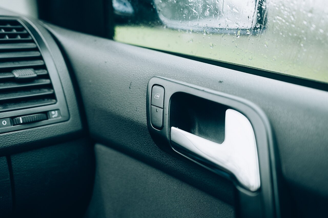 Reference photograph of Close-up view of a car door handle showing details during a rainy day