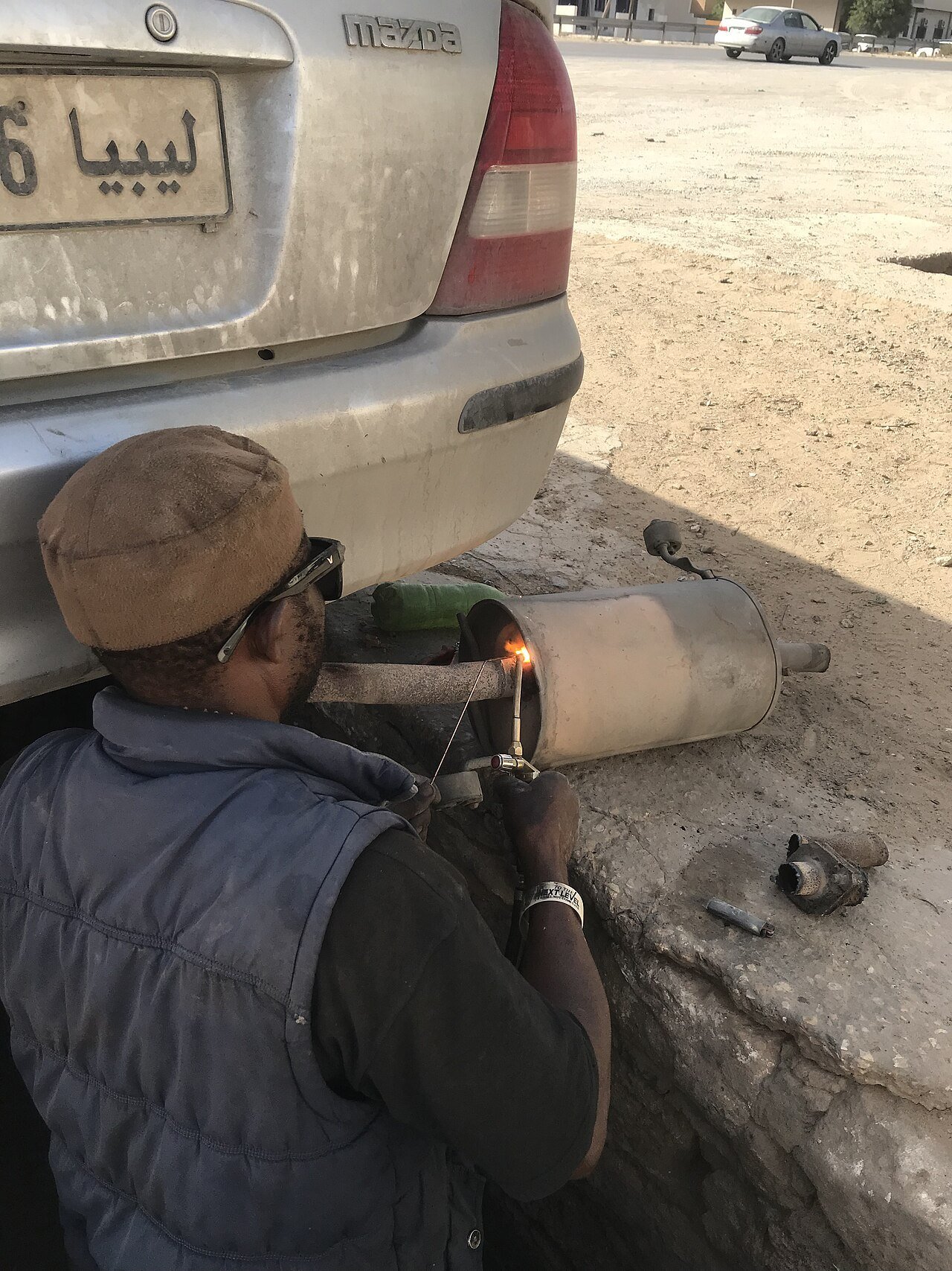 Real workshop photograph of a technician working on a vehicle exhaust system