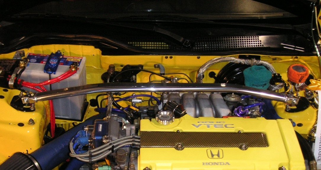 Real photograph of a red strut tower brace in a compact car engine bay